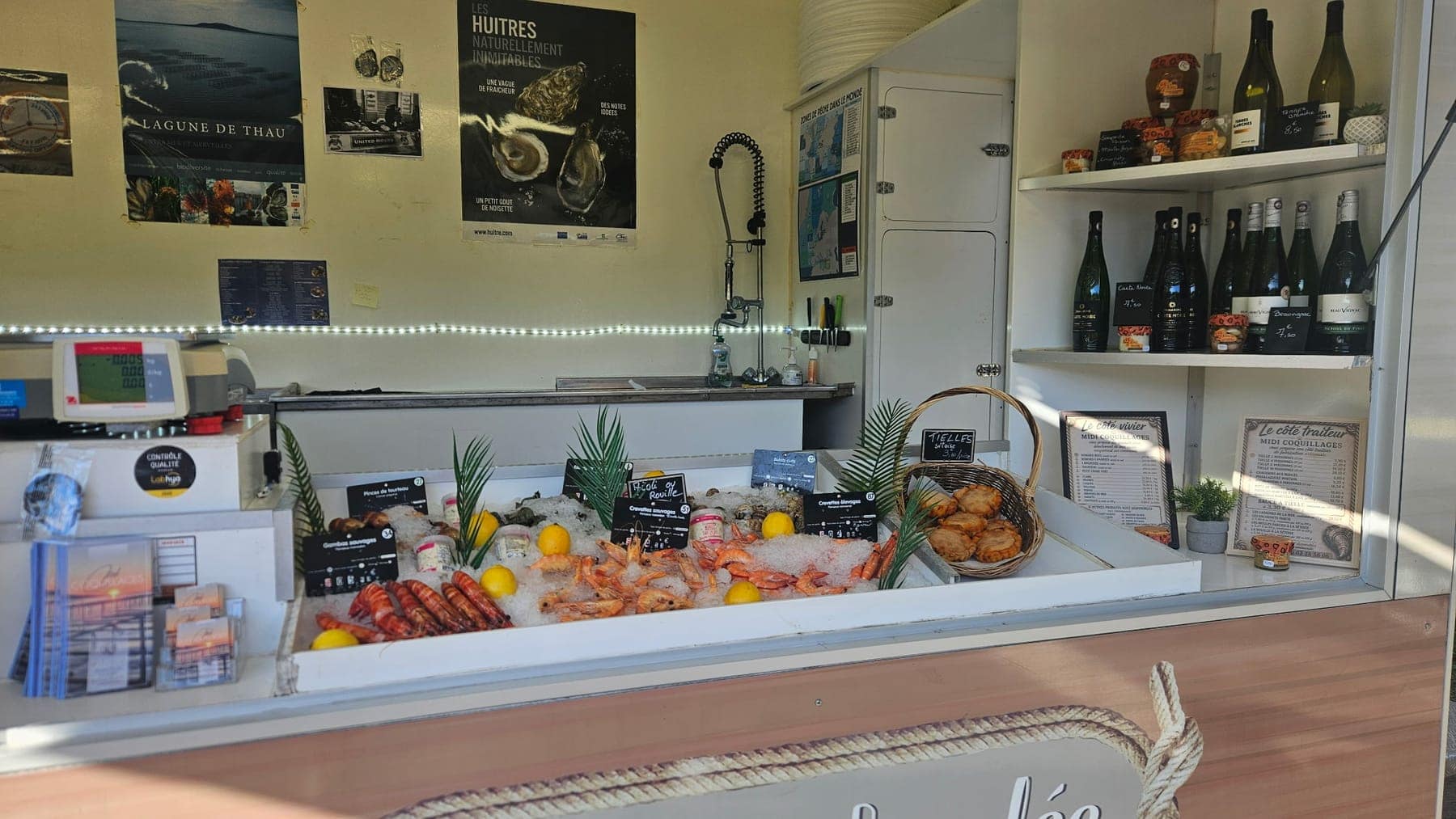 Étal de Midi Coquillages au marché : gambas, crevettes sur glace, tielles et vins